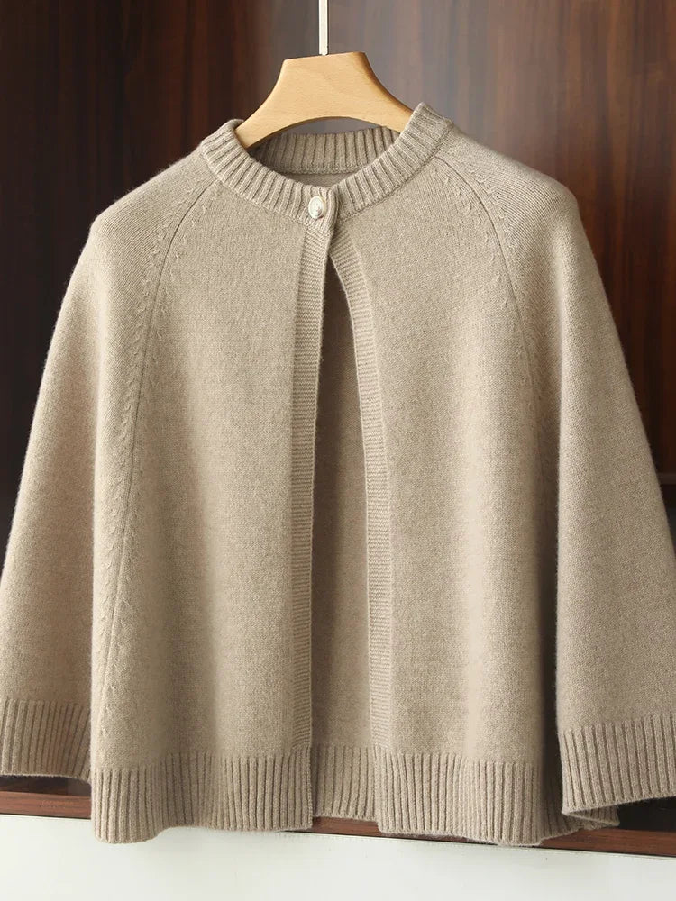 Beige knitted cape on a wooden hanger against a wooden background