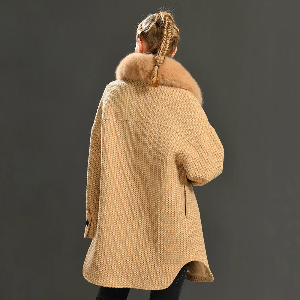 Person wearing a beige knitted coat with fur collar on a dark background