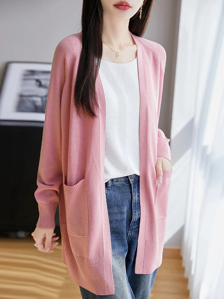 Person wearing a pink cardigan over a white shirt and blue jeans indoors.