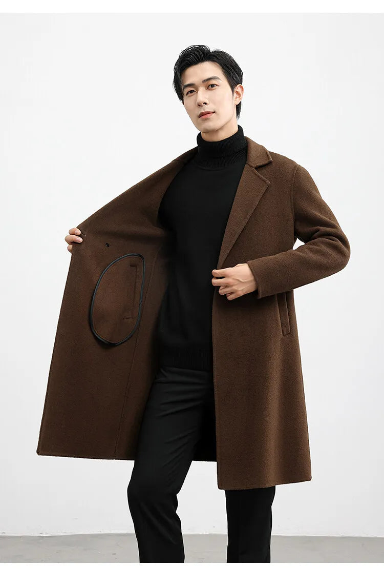 Man wearing a brown coat over a black turtleneck and pants on a white background