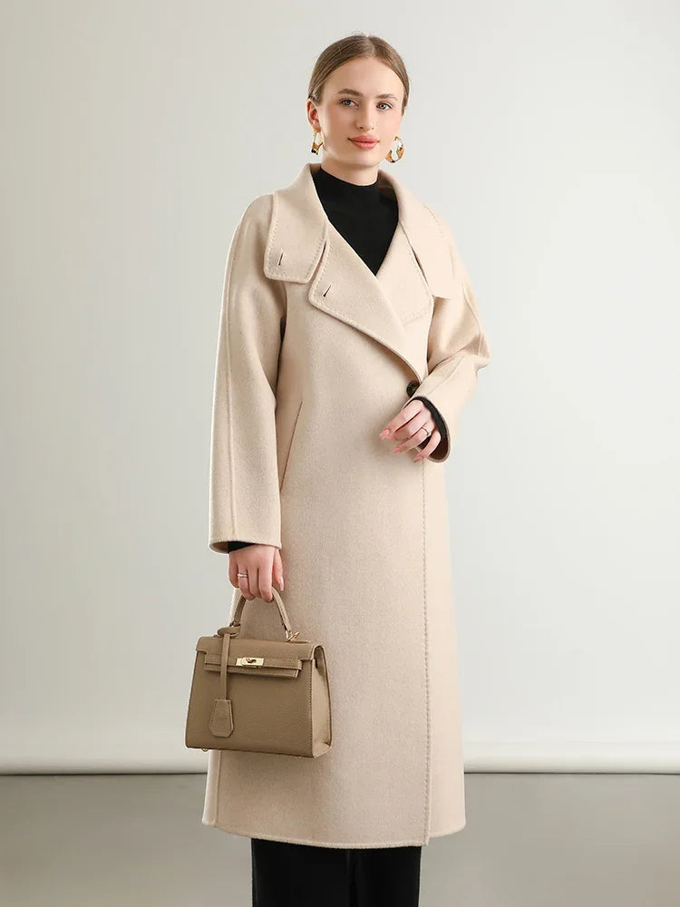 Woman wearing a beige coat holding a matching handbag against a plain background
