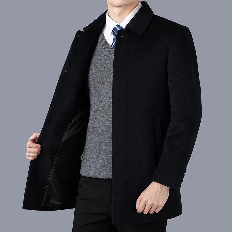 Man wearing a black coat over a gray sweater and white shirt on a gray background