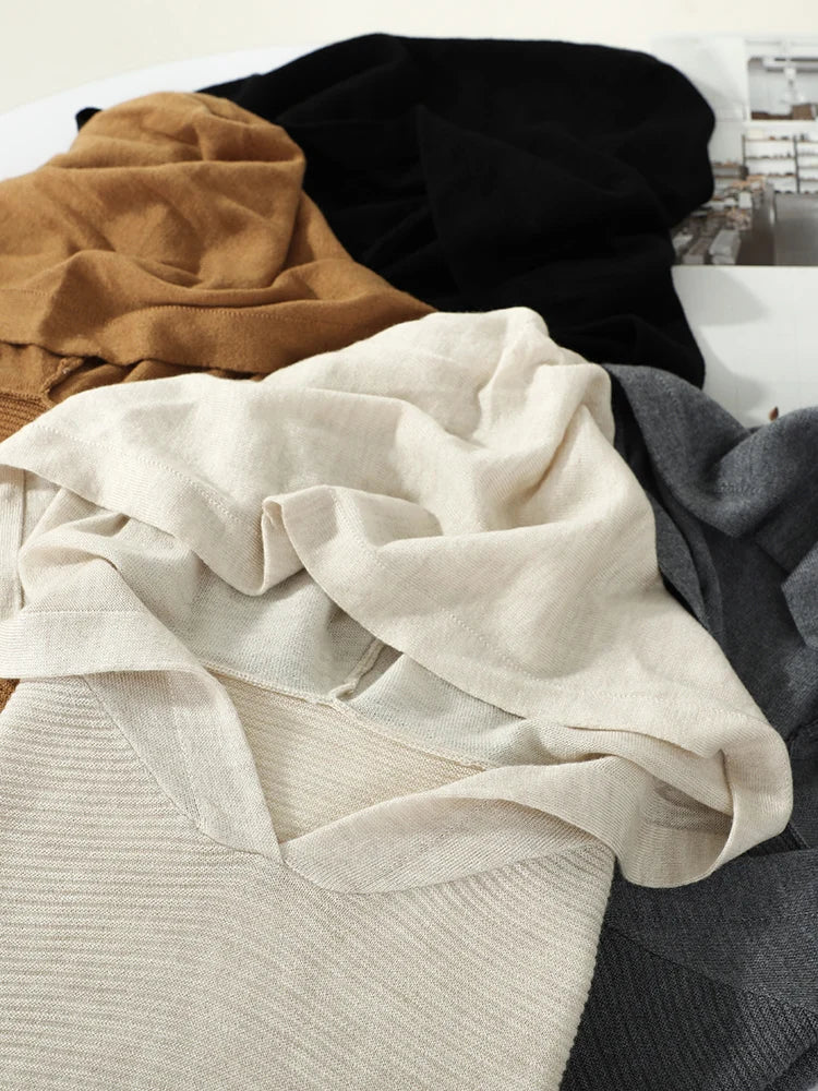 Stack of folded sweaters in beige, black, and gray on a white surface.