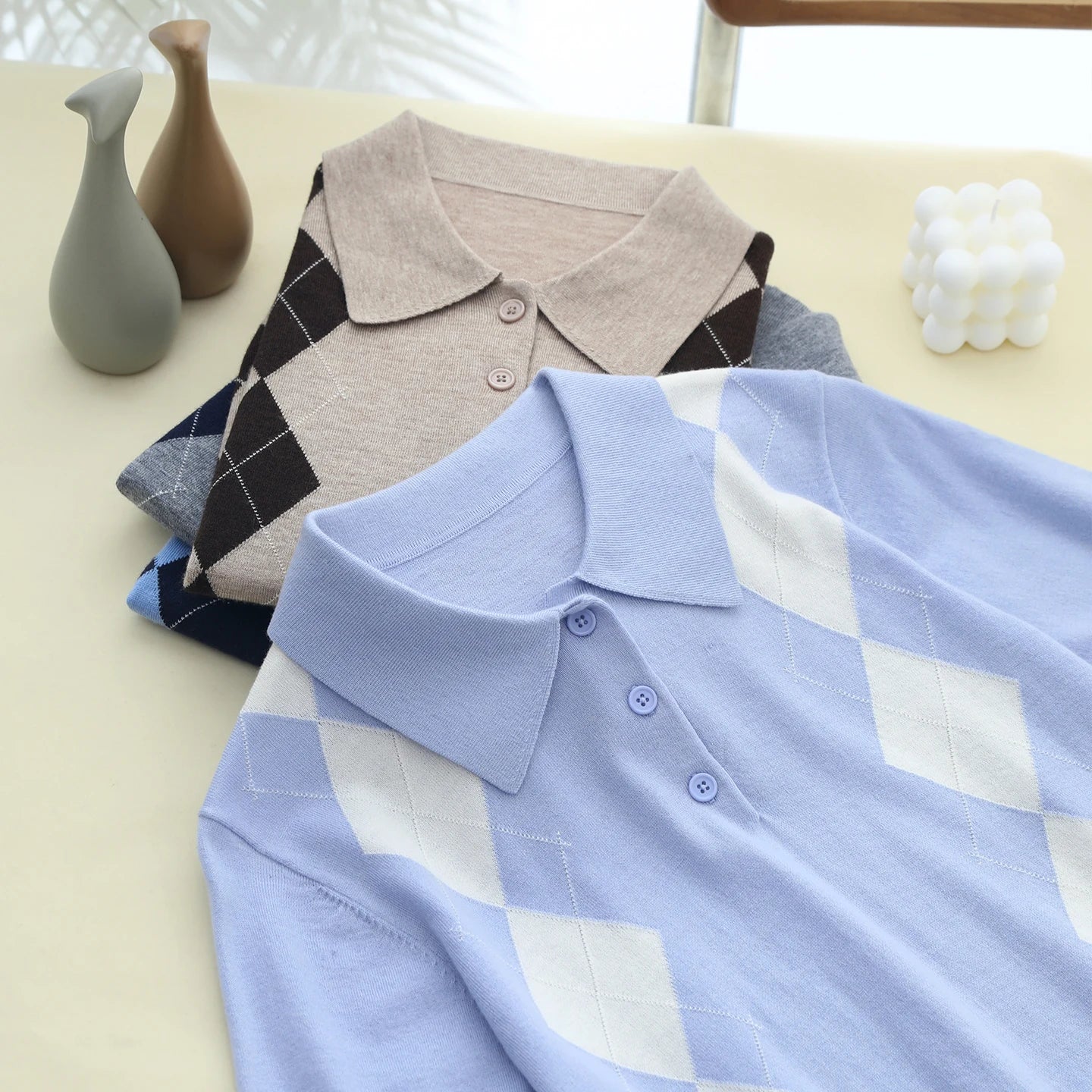 Stack of folded shirts on a light surface with decorative vases in the background