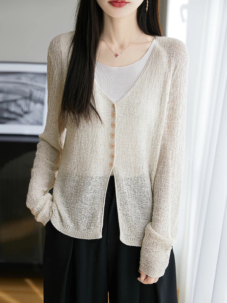 Woman wearing a beige cardigan over a white top and black pants indoors.