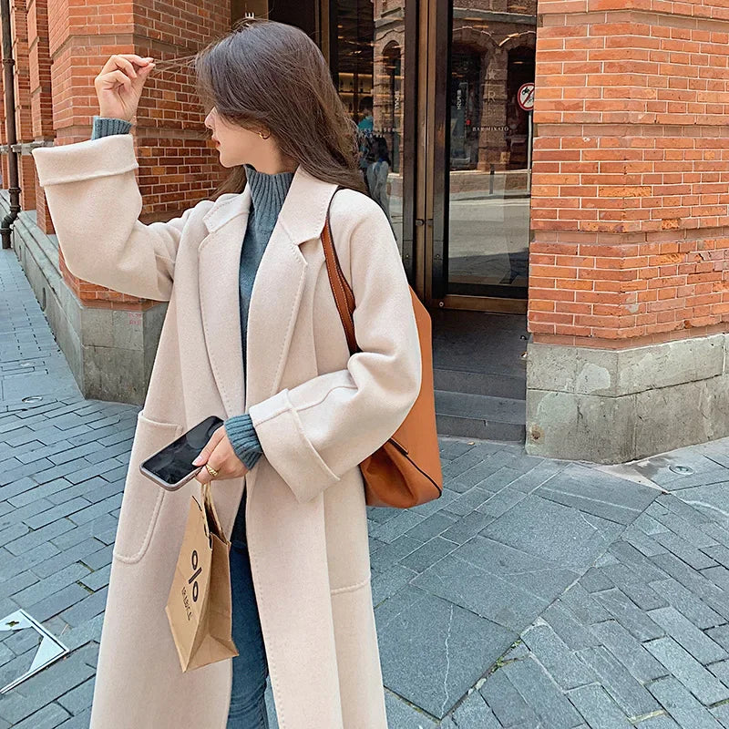 Woman in a beige coat taking a selfie on a city street.