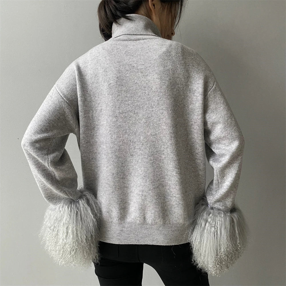 Person wearing a light gray sweater with textured cuffs on a plain background
