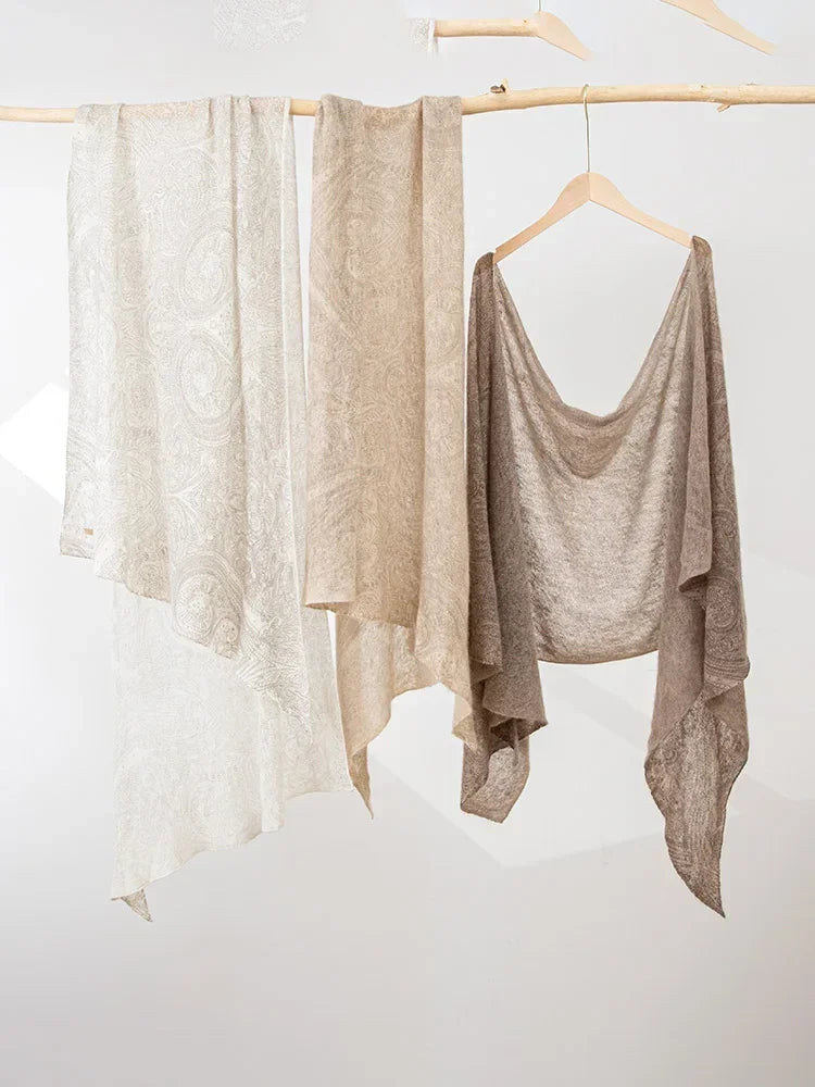 Three beige and brown garments hanging on a wooden rod against a white background