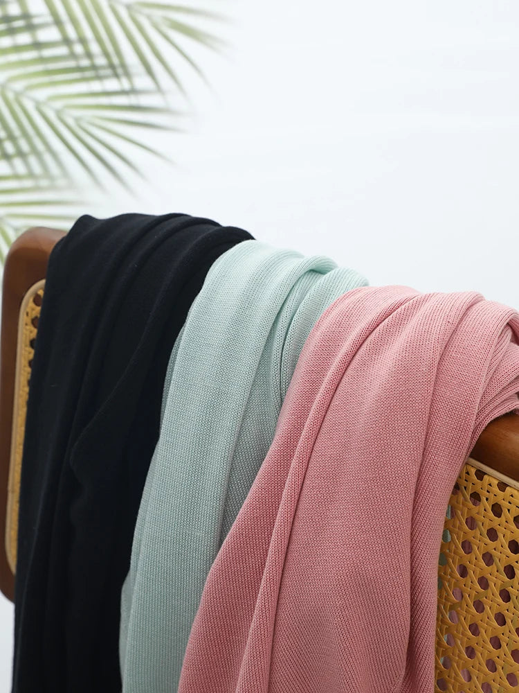 Three scarves in black, green, and pink draped over a chair with a blurred natural background.
