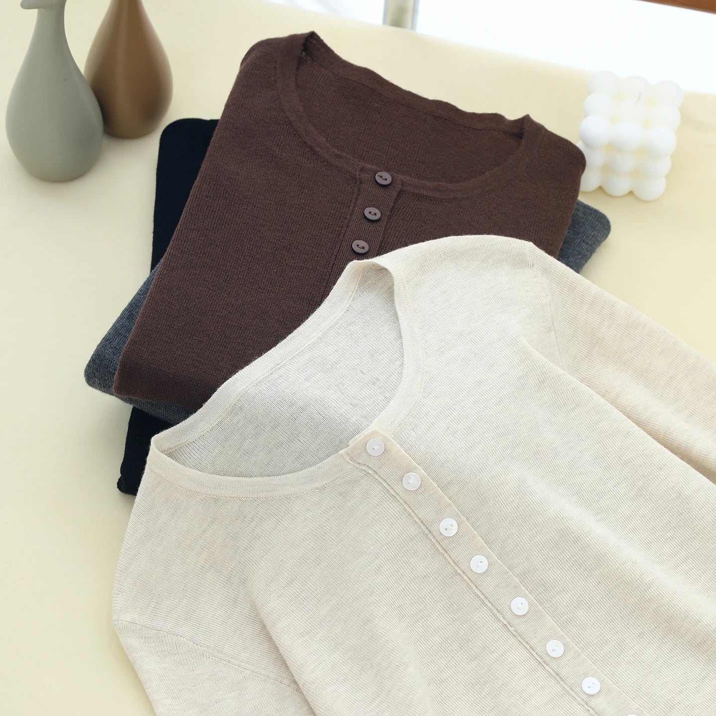 Two shirts, one brown and one beige, on a light surface with decorative items.