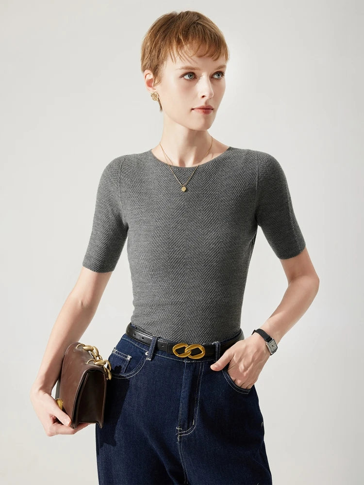 Woman wearing a gray short-sleeve top and blue jeans, holding a brown handbag on a light background