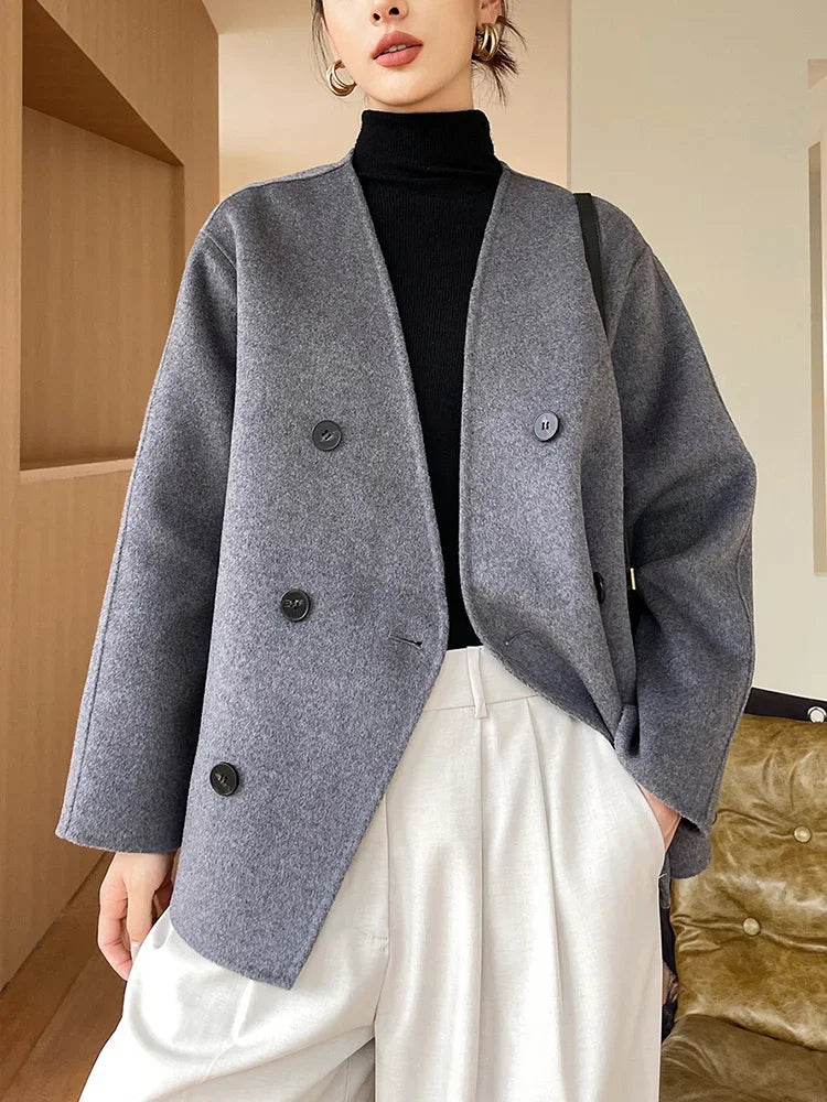 Person wearing a gray coat over a black turtleneck and white pants indoors.