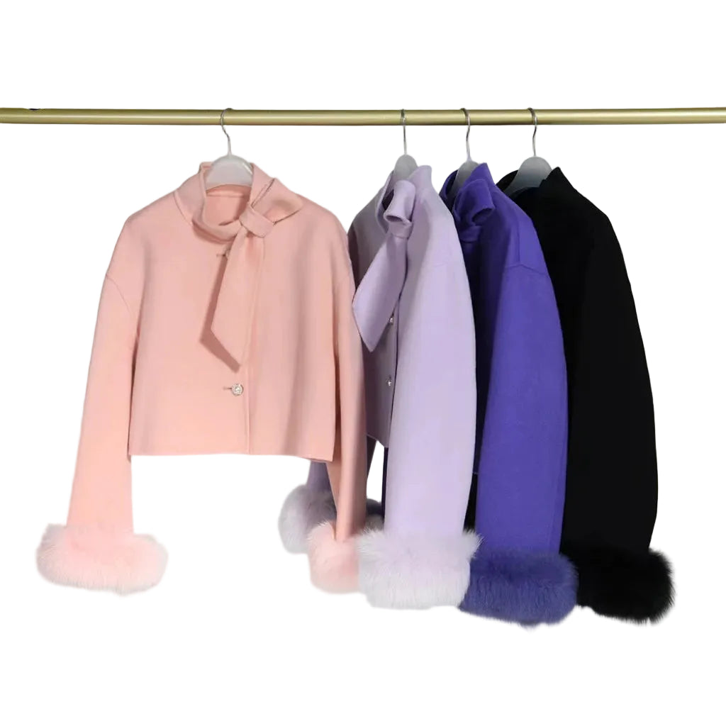 Four coats in pink, purple, and black with fur cuffs on a rack against a gray background.