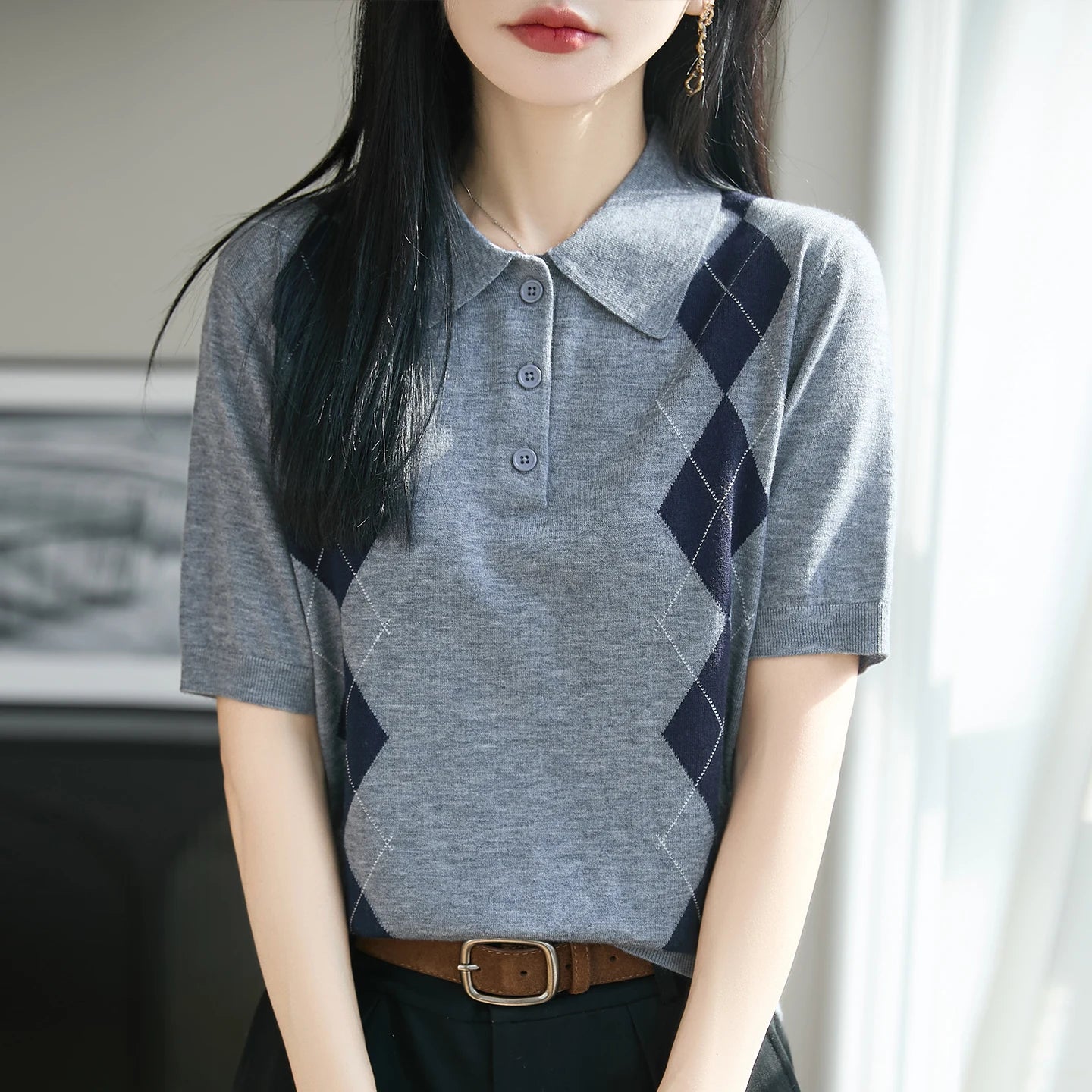 Person wearing a gray and navy argyle patterned polo shirt indoors.