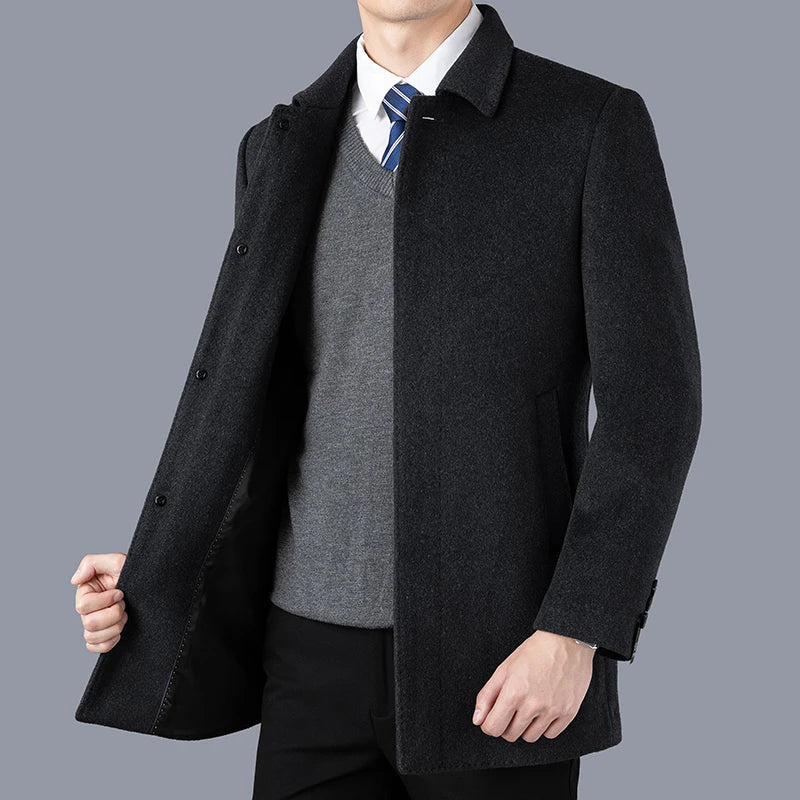 Man wearing a dark gray coat over a suit and tie on a gray background