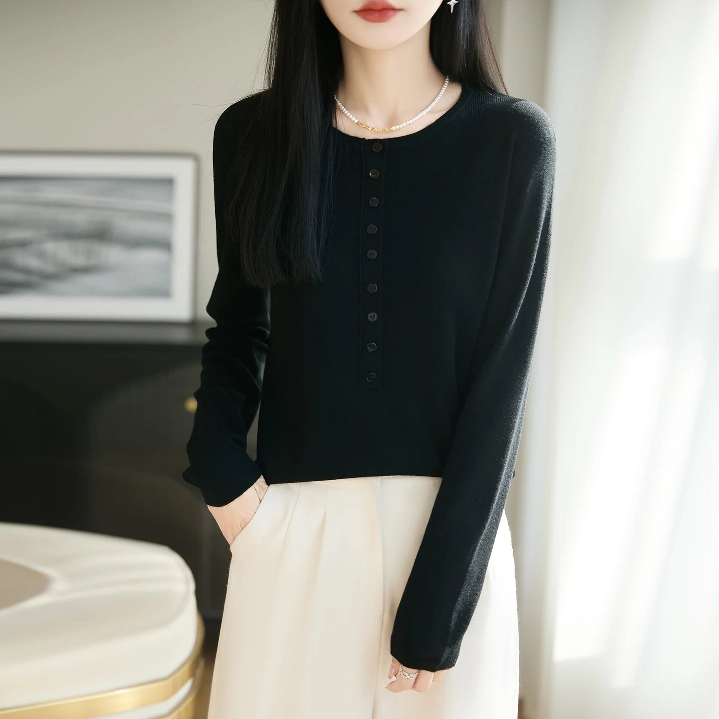 Person wearing a black long-sleeve top and white pants in an indoor setting