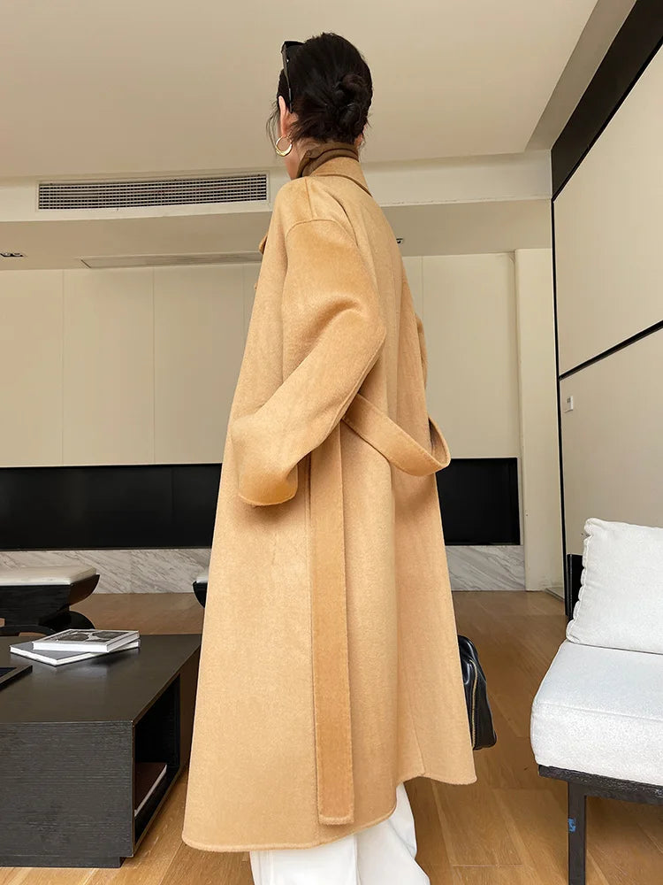 Person wearing a beige coat in a modern room with neutral decor.