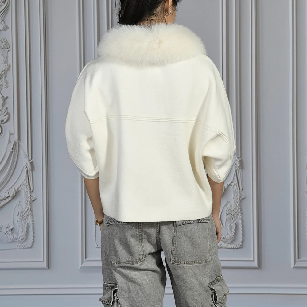 Person wearing a white coat with fur collar against a decorative wall.