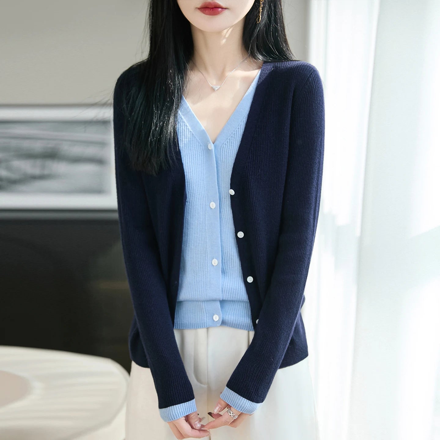 Woman wearing a navy cardigan over a light blue shirt with white pants.