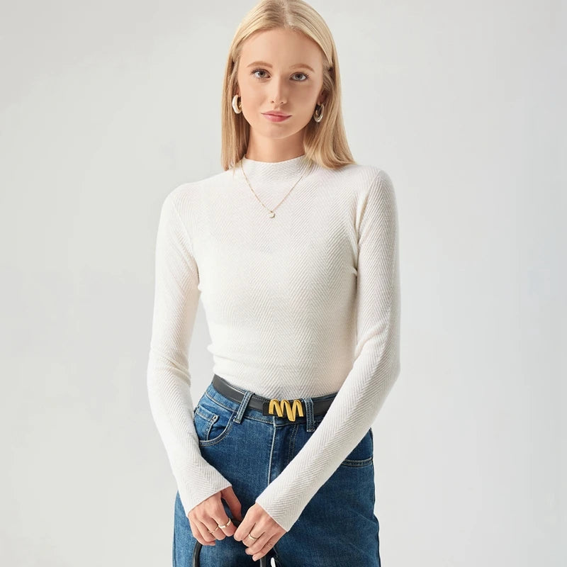 Woman wearing a white long-sleeve top and blue jeans on a plain background