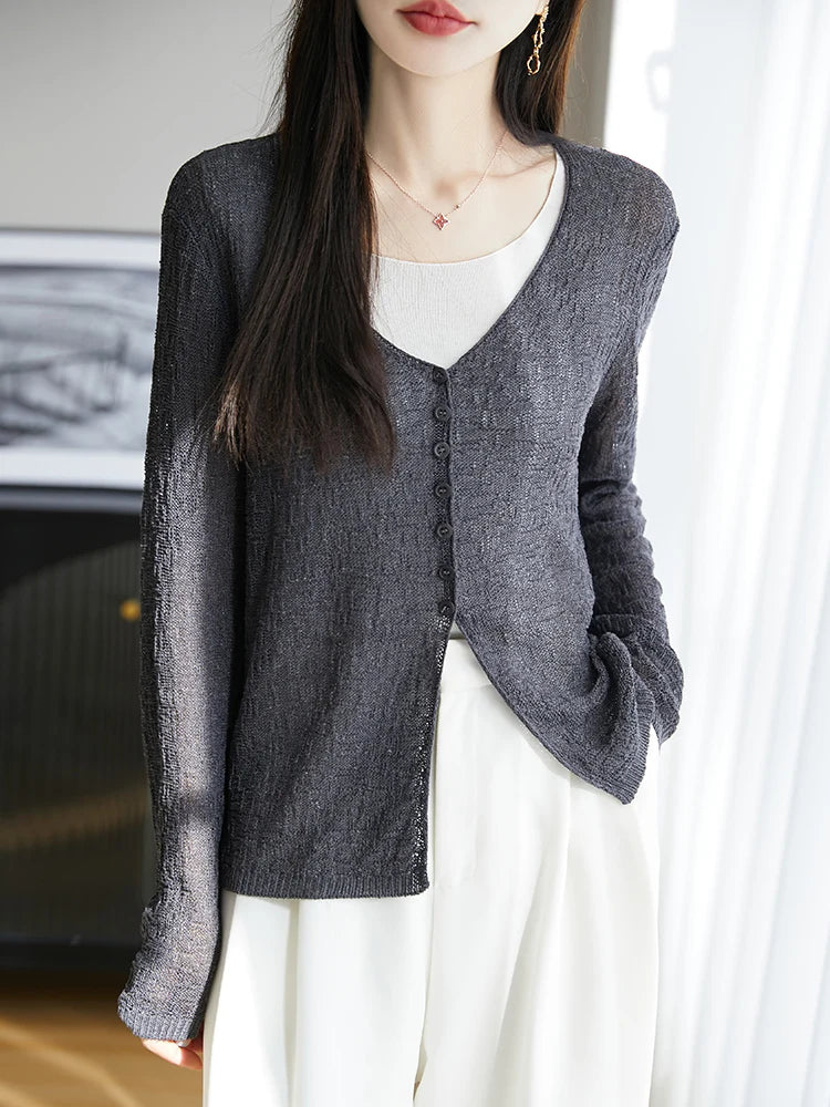 Person wearing a gray cardigan over a white shirt and pants indoors.