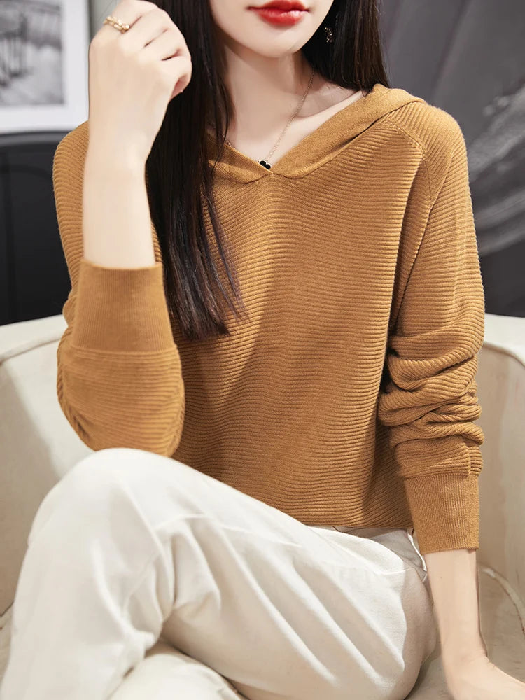 Person wearing a brown ribbed sweater and white pants sitting on a couch.
