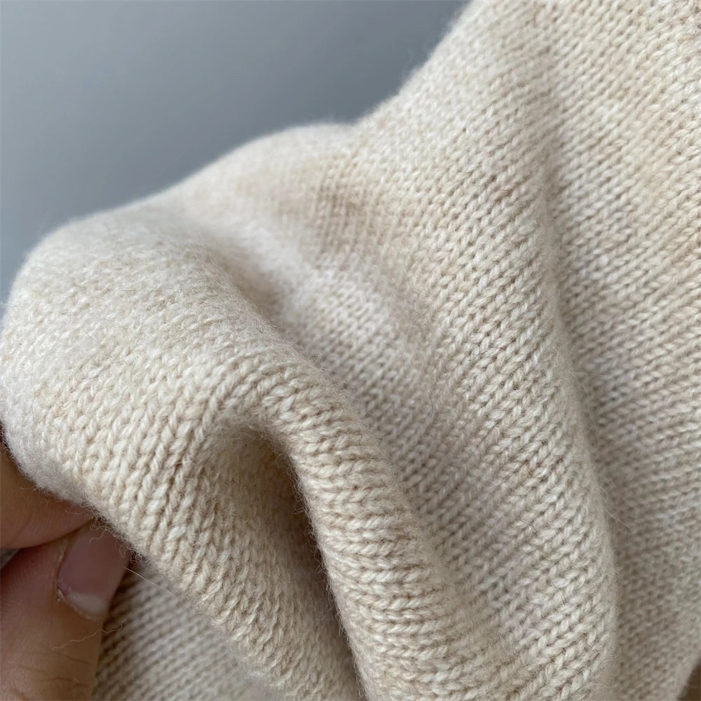 Close-up of beige knitted fabric held by a hand against a gray background
