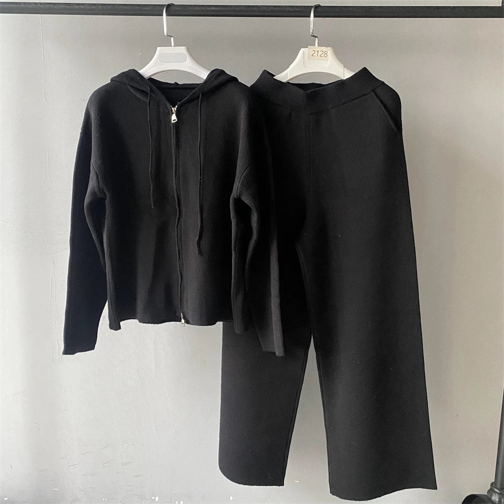 Black hoodie and pants set on hangers against a plain background