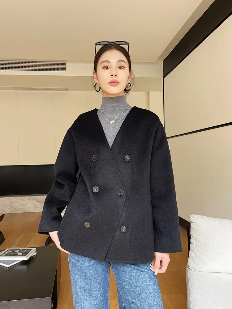Person wearing a black coat over a gray turtleneck and blue jeans indoors.