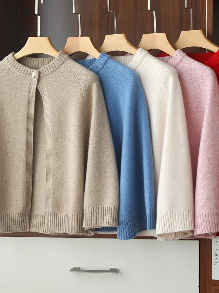 Row of colorful sweaters on hangers against a wooden wall.