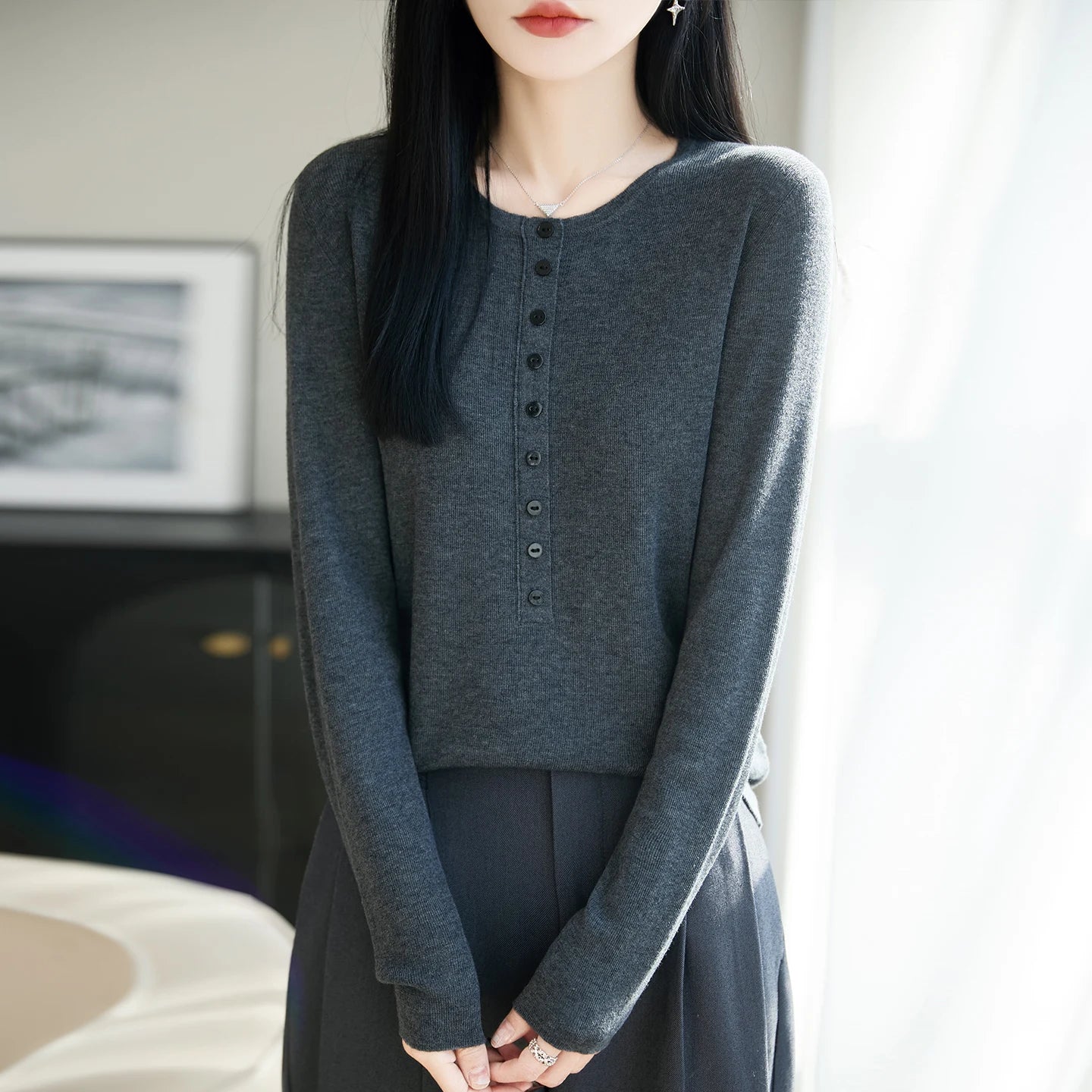 Person wearing a gray long-sleeve top with buttons in an indoor setting