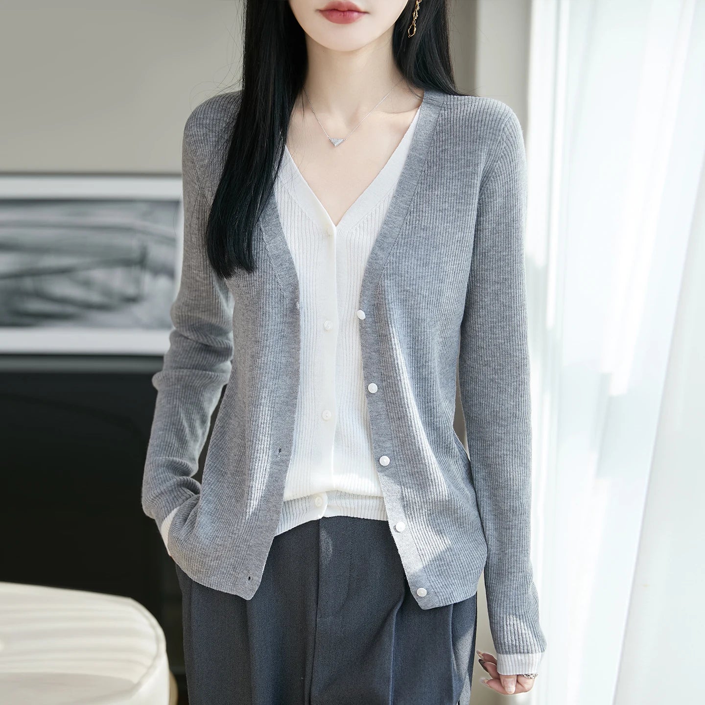 Person wearing a gray cardigan over a white shirt and dark pants indoors.
