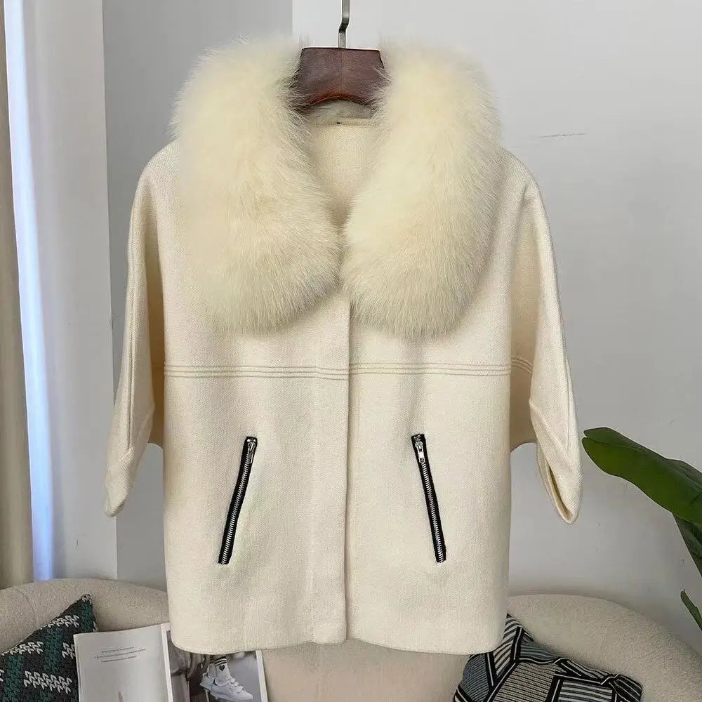 Cream-colored coat with fur collar on a hanger against a white wall.