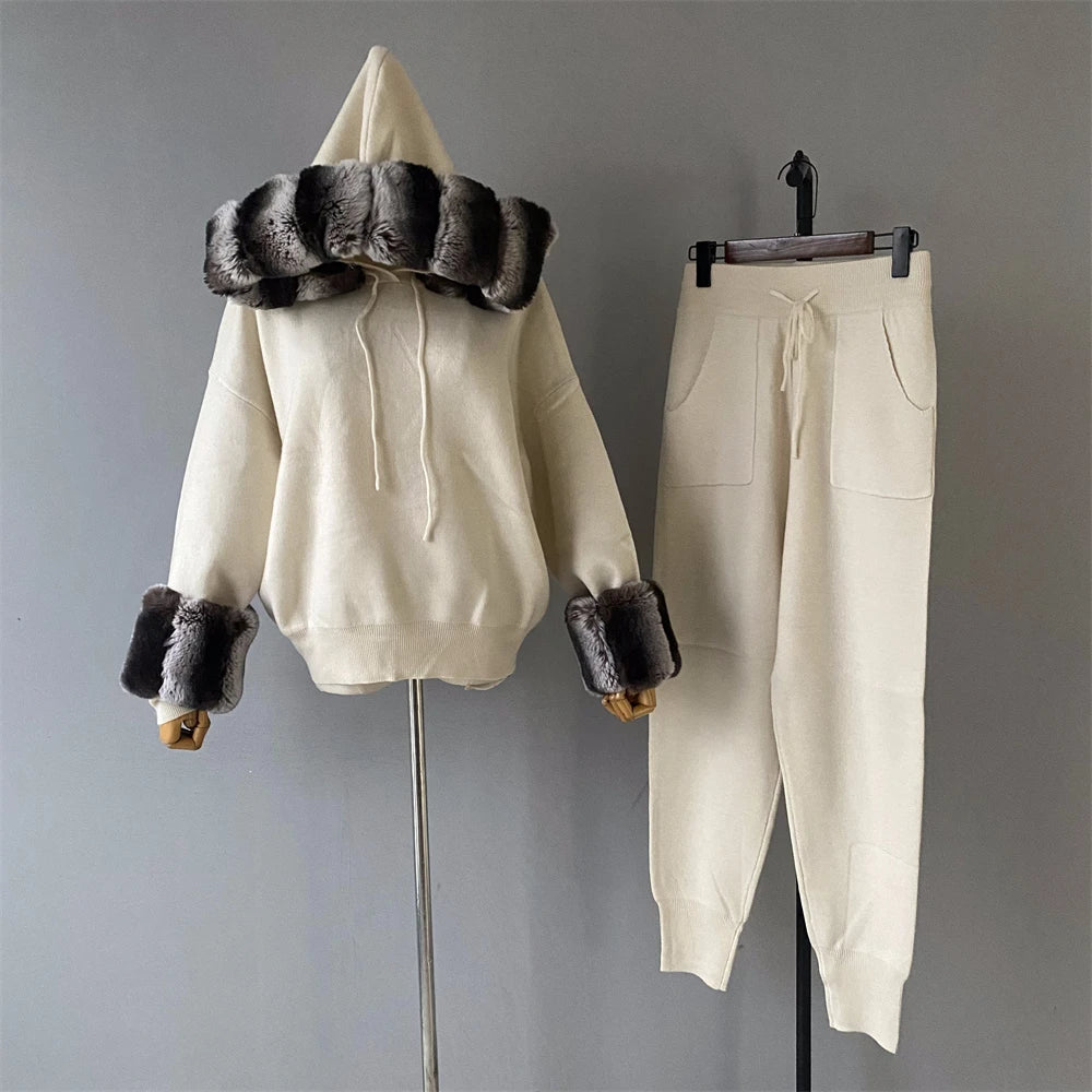 White hoodie with fur trim and matching pants on hangers against a gray background