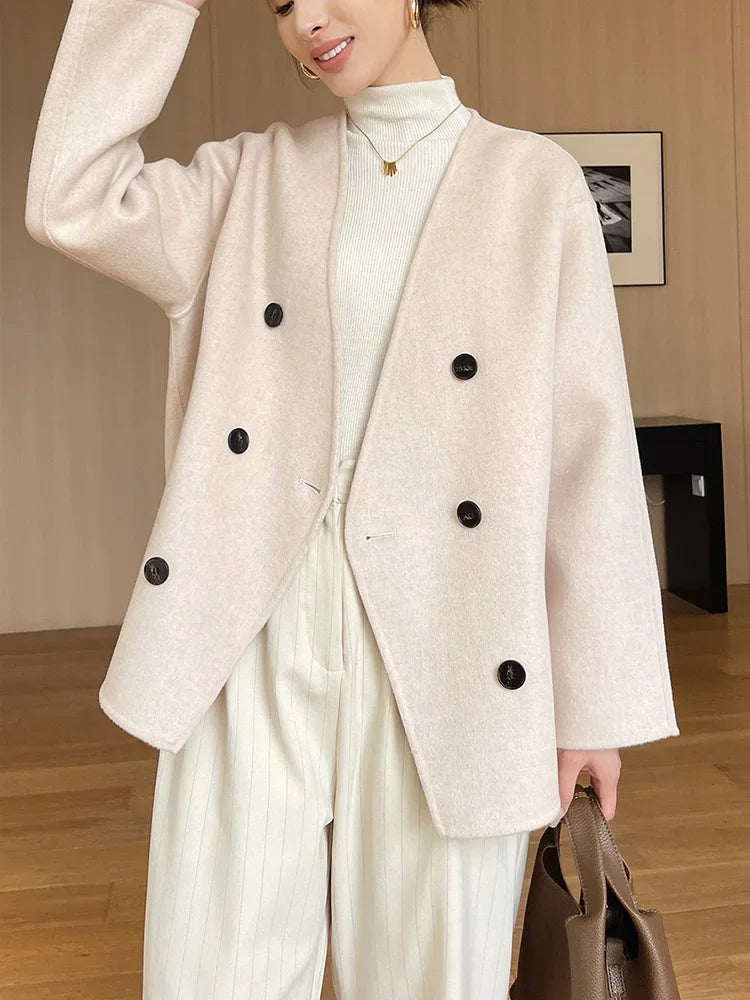 Person wearing a beige blazer with black buttons in an indoor setting