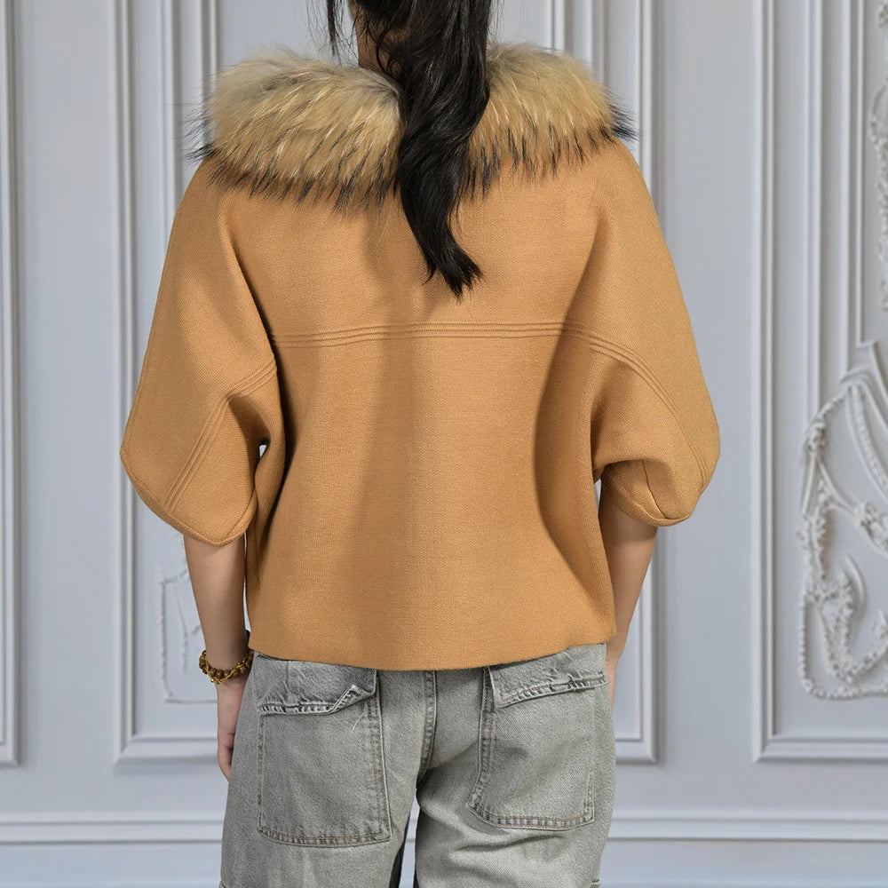 Person wearing a tan coat with a fur collar against a decorative white wall.