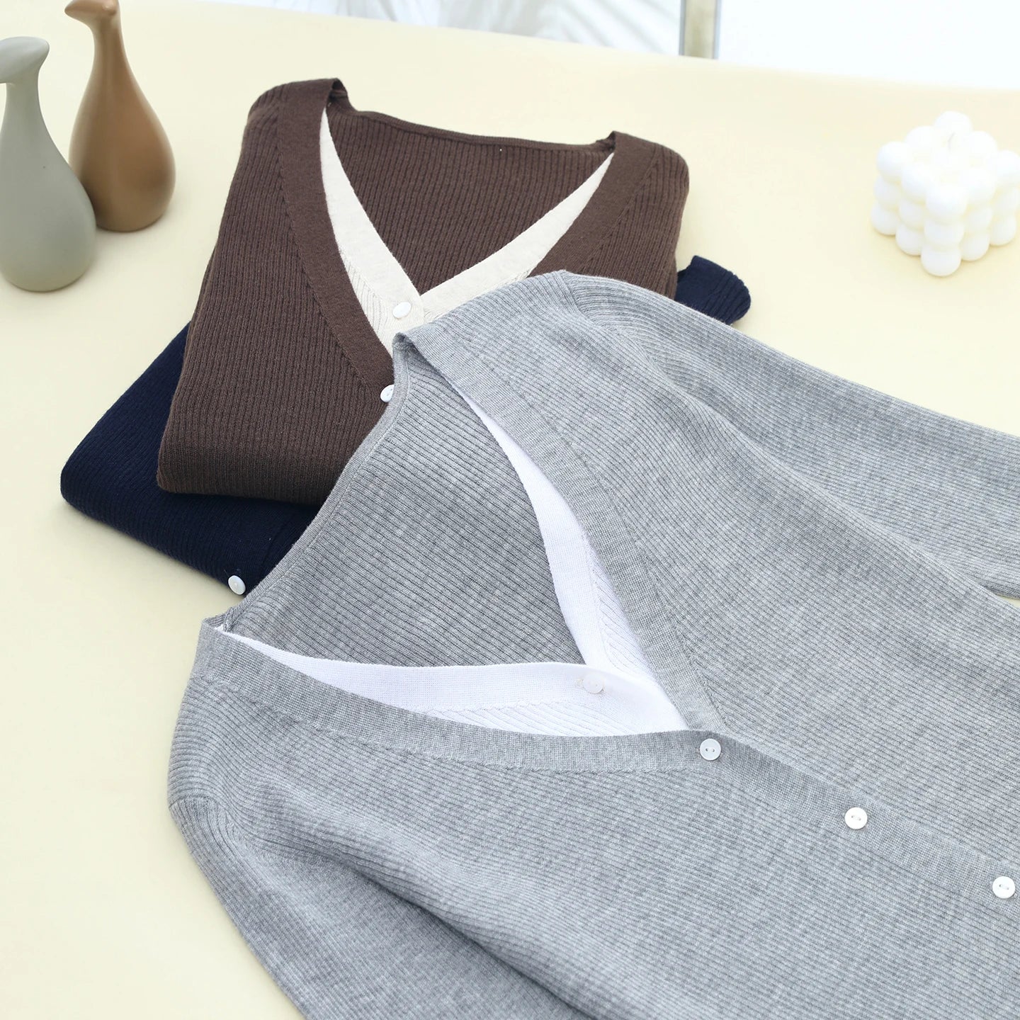 Three sweaters in brown, navy, and gray on a light surface.