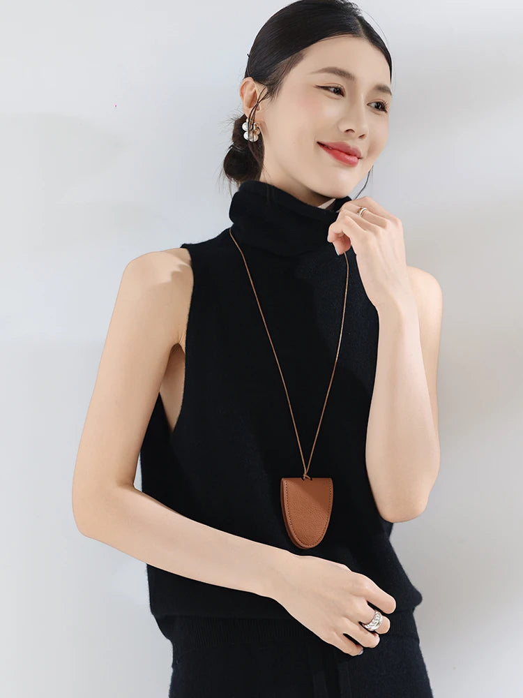 Woman wearing a black sleeveless top with a long necklace against a white background