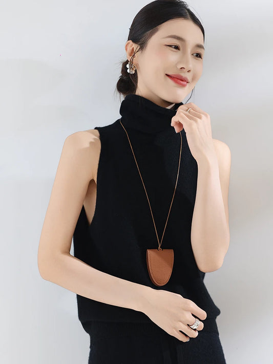 Woman wearing a black sleeveless top with a long necklace against a white background