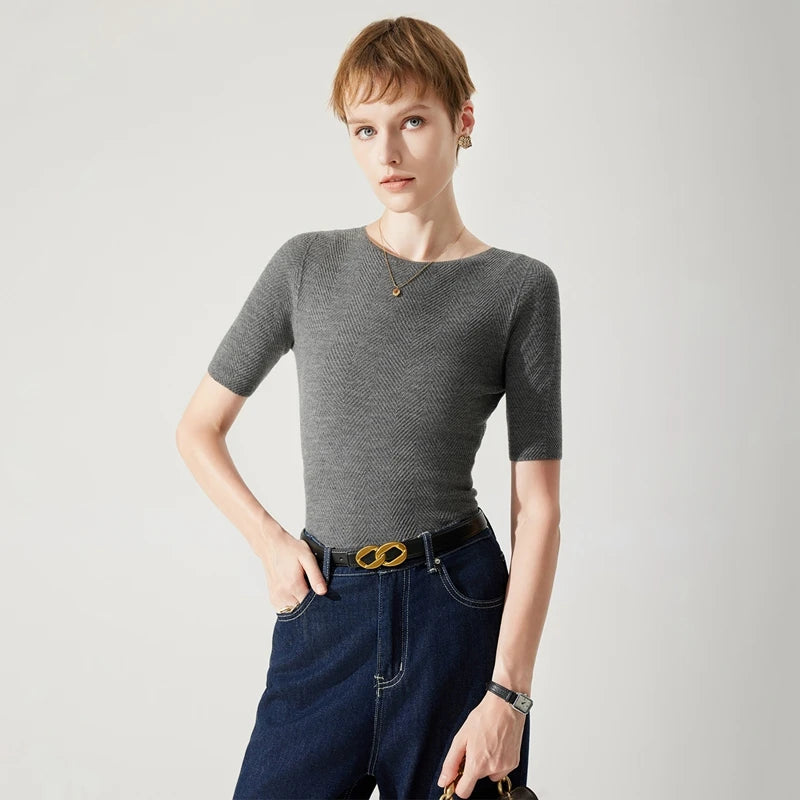Woman wearing a gray textured top and blue jeans with a gold belt on a light gray background