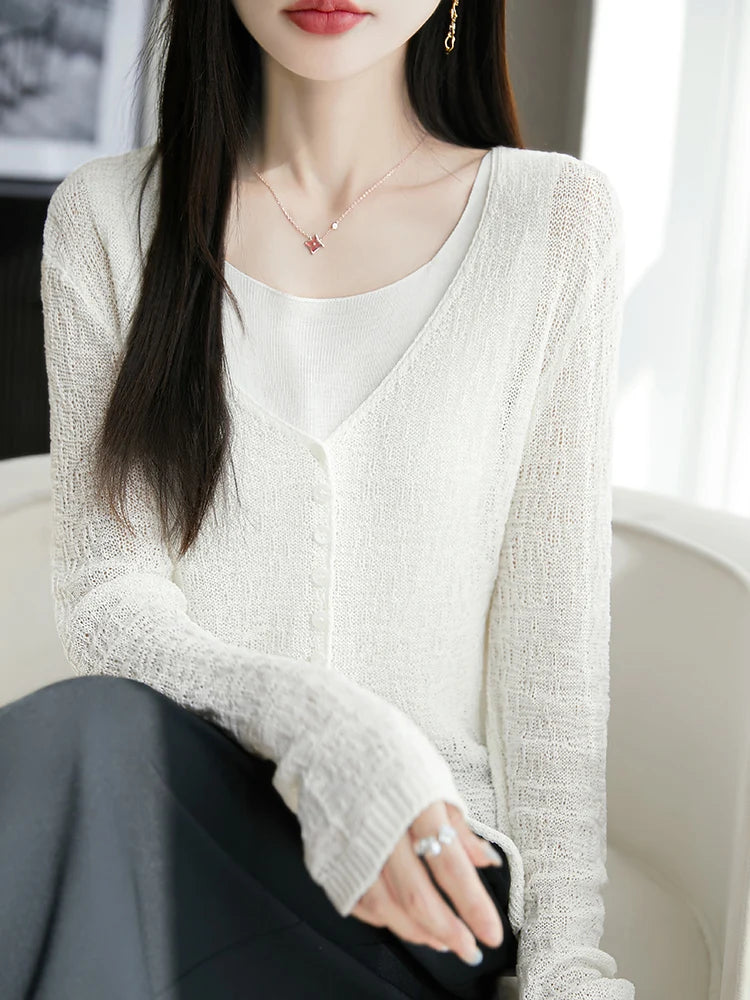 Woman wearing a light-colored cardigan over a white top, sitting on a couch.