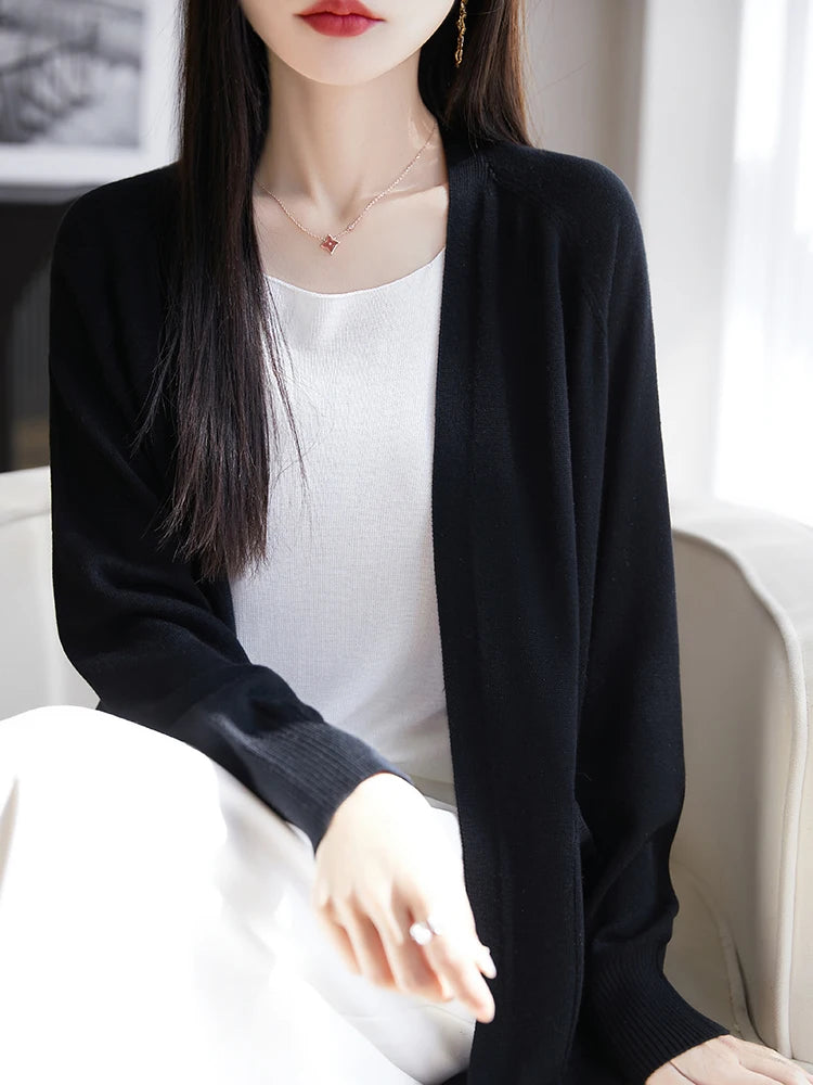 Person wearing a black cardigan over a white top, sitting on a white couch.
