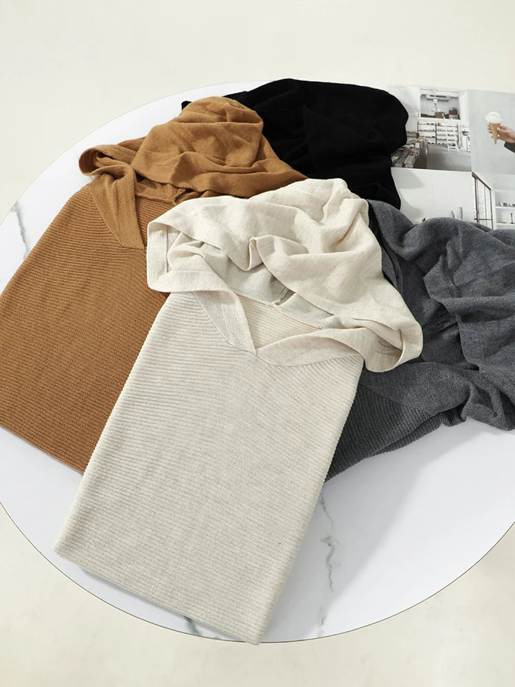 Four folded sweaters in brown, black, beige, and gray on a white marble surface.