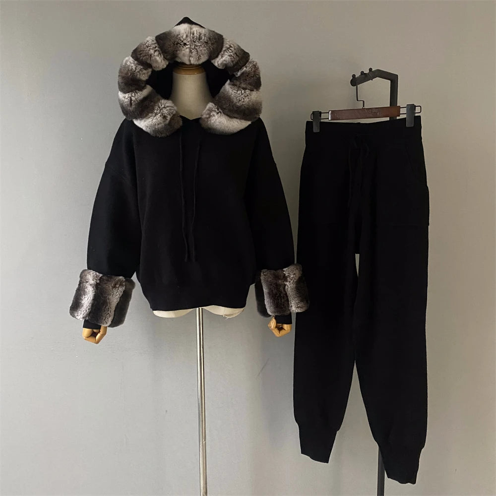 Black hoodie with fur trim on a mannequin and black pants on a hanger against a plain background
