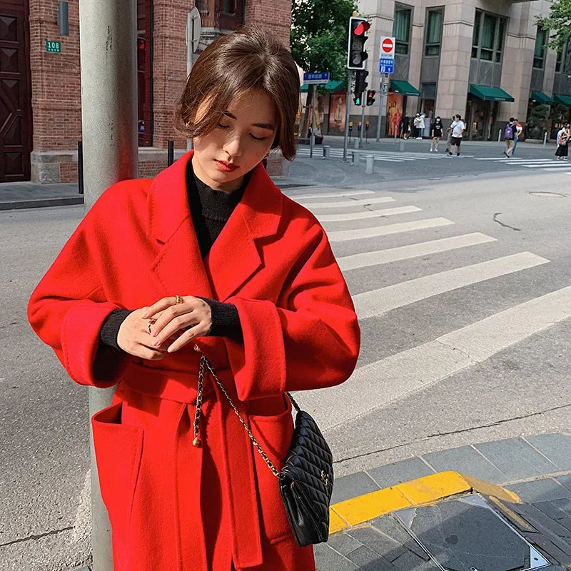 Woman in a red coat standing on a city street corner.
