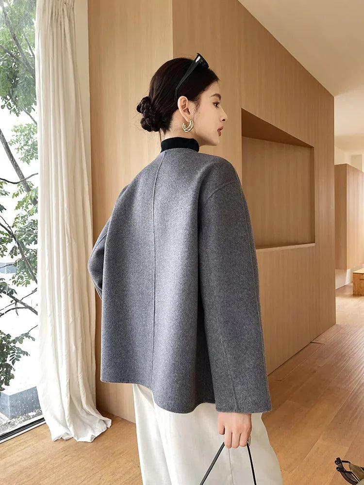 Woman wearing a gray coat in a modern indoor setting with wooden walls and white curtains.