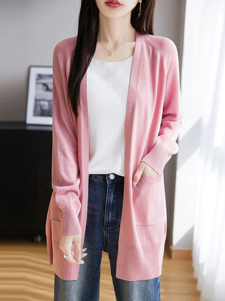 Person wearing a pink cardigan over a white shirt and blue jeans indoors.