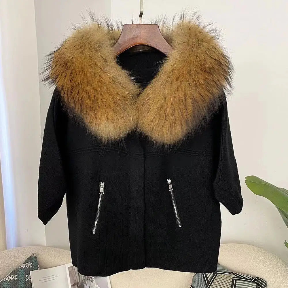 Black coat with a large fur collar on a hanger against a white wall.
