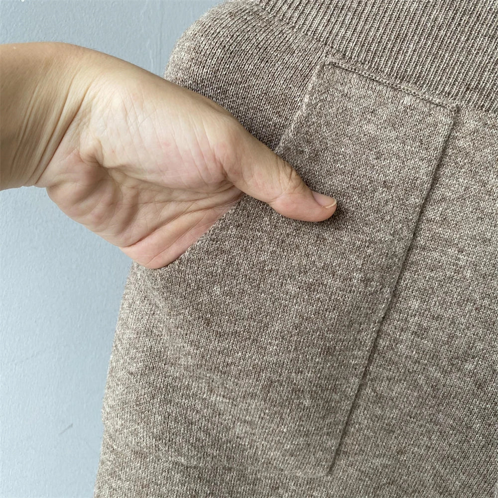 Hand pointing to a pocket on a brown fabric garment against a light blue background