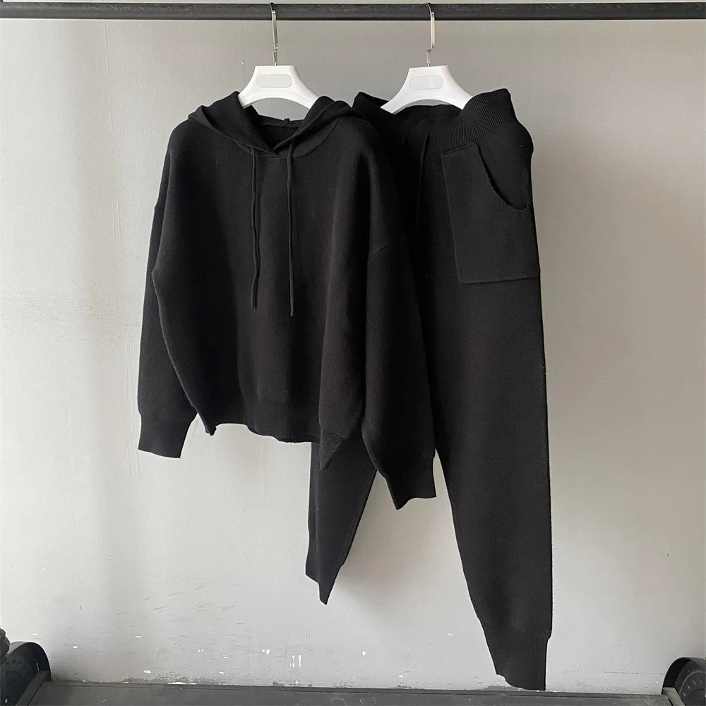 Black hoodie and pants set on hangers against a plain background